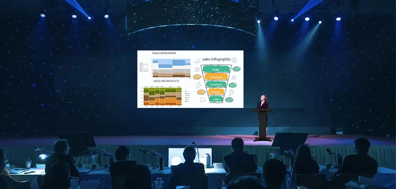 Professional presenting at corporate event in auditorium using digital podium and LED display.